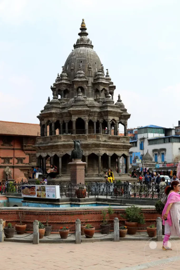 Das Bild zeigt den beeindruckenden Krishna Mandir Tempel am Durbar Square in Patan, Nepal. Menschen sitzen auf den Stufen und am Rand des Wasserelements, das den Tempel umgibt, was eine friedliche und belebte Atmosphäre erzeugt. Die Architektur des Tempels und die dargestellte Szene fangen die kulturelle Essenz des Ortes ein.