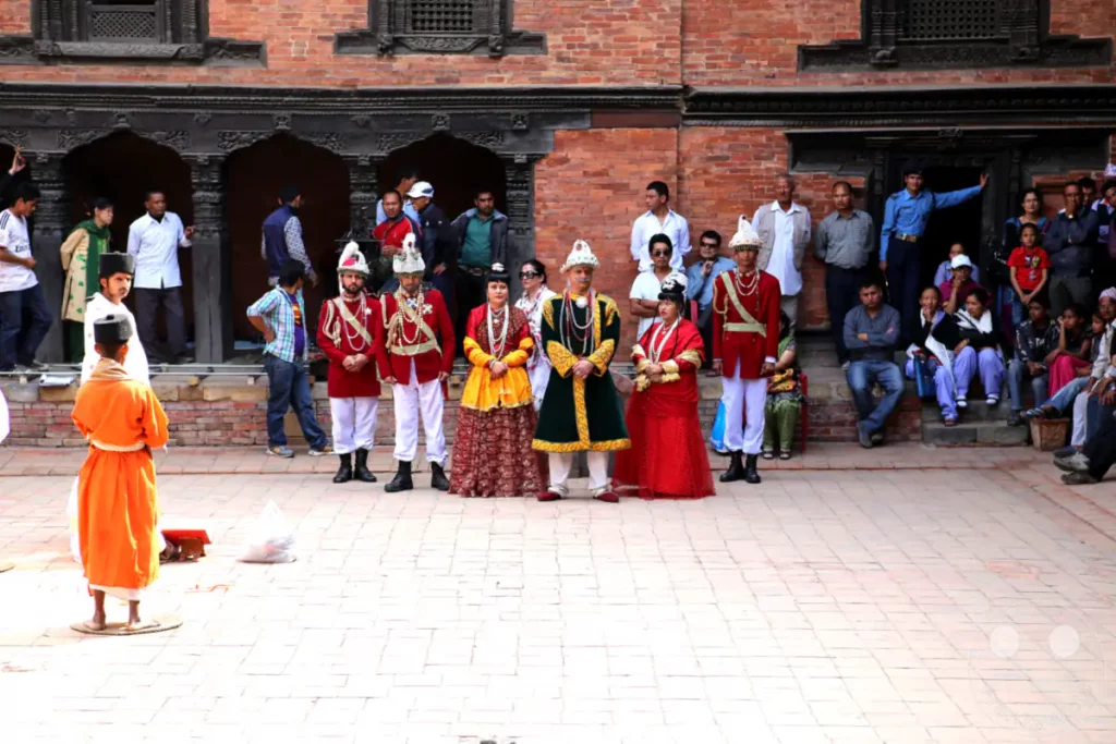 Eine Gruppe von Personen in traditioneller Kleidung posiert auf dem Durbar Square in Patan, Nepal. Der historische Platz dient als Kulisse für die festliche Szene, die von der traditionellen Architektur und den farbenfrohen Gewändern geprägt ist.