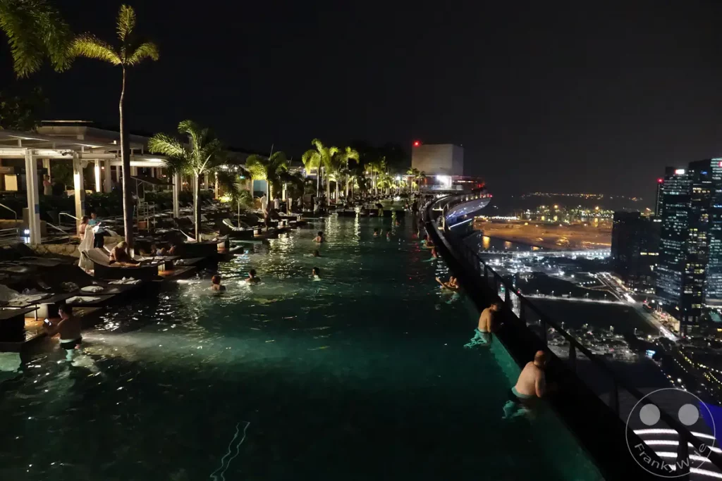 Ein atemberaubender Infinity-Pool auf dem Dach des Marina Bay Sands Hotels in Singapur bietet bei Nacht einen spektakulären Blick auf die Stadt. Zahlreiche Gäste genießen das kühle Nass vor der Kulisse der beleuchteten Skyline. Die Szene strahlt eine Atmosphäre von Entspannung und luxuriösem Nachtleben aus.