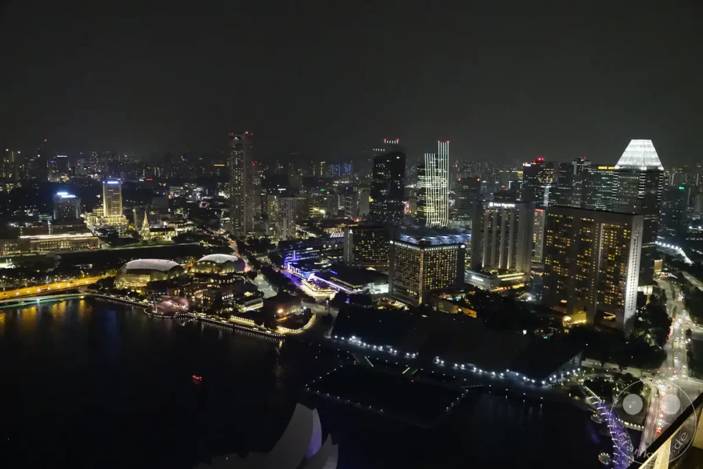 Die Skyline von Singapur im Glanz der Nacht, beleuchtet von unzähligen Lichtern der Wolkenkratzer und Gebäude entlang der Marina Bay. Der dunkle Himmel bildet einen starken Kontrast zu den hell erleuchteten Straßenzügen und Wasserwegen, die die Stadt lebendig wirken lassen. Eine beeindruckende Panoramaaufnahme, die die pulsierende Energie und moderne Architektur Singapurs einfängt.