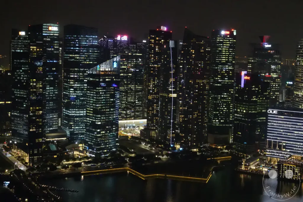 Die Skyline von Singapur erstrahlt bei Nacht in einem Meer aus Lichtern. Zahlreiche Wolkenkratzer sind hell erleuchtet und spiegeln sich im dunklen Wasser wider. Die beleuchteten Gebäude und die Lichter des Hafens schaffen eine beeindruckende und lebendige Atmosphäre in der Metropole.