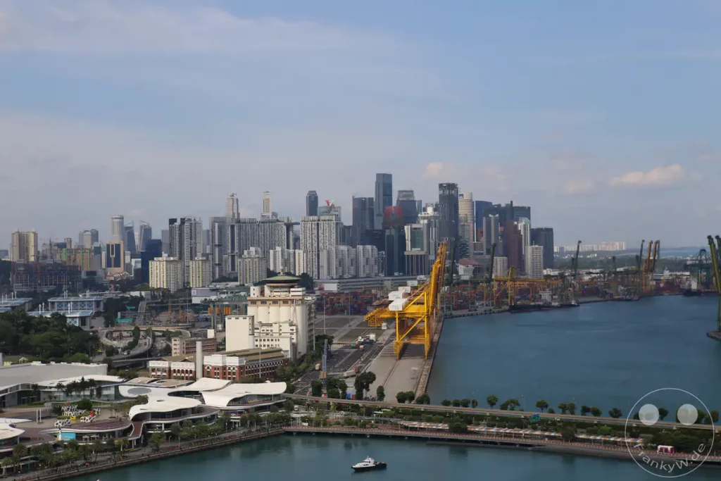 Ein Panorama über Singapurs beeindruckende Skyline und einen geschäftigen Hafen. Die Szene wird von hohen Gebäuden und weitläufigen Industrieanlagen mit großen Kränen und Containern dominiert. Das Bild vermittelt die Energie und die wirtschaftliche Bedeutung der Hafenstadt.