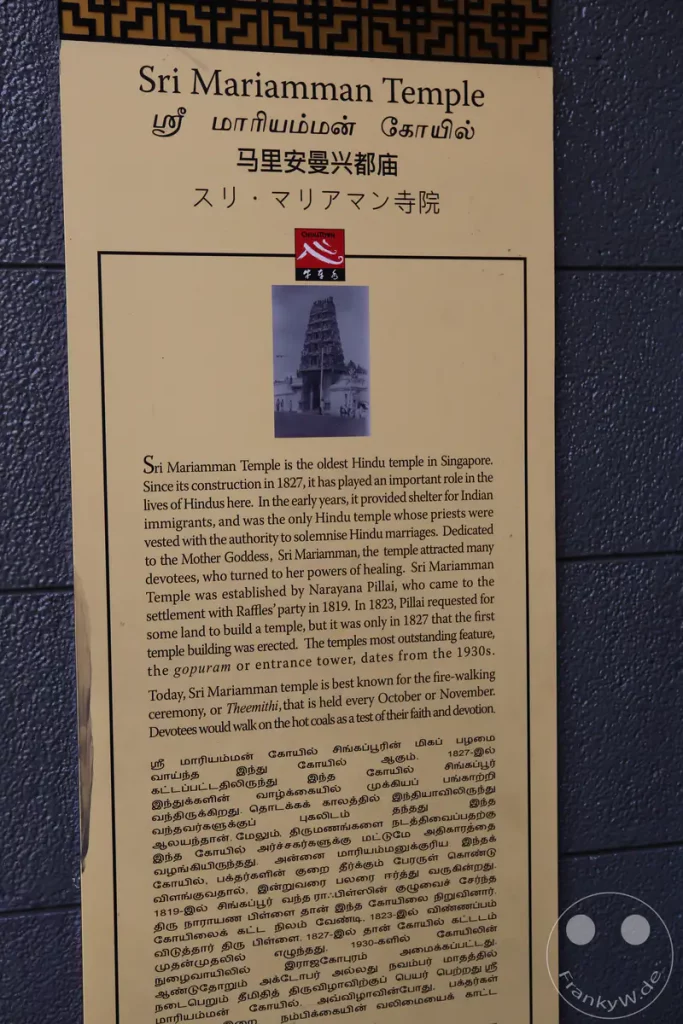 Das Bild zeigt eine Informationstafel über den Sri Mariamman Tempel in Singapur, den ältesten Hindu-Tempel der Stadt. Die Tafel enthält sowohl englischen als auch tamilischen Text und hebt die Bedeutung des Tempels für die hinduistische Gemeinschaft hervor. Eine historische Fotografie des Tempels vervollständigt die Darstellung und unterstreicht die architektonische Pracht.