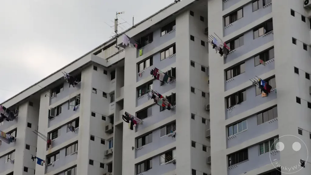 Ein mehrstöckiges Wohngebäude in Singapur, an dessen Fassade zahlreiche Wäscheleinen mit hängender Kleidung angebracht sind. Die Fenster des Gebäudes sind teilweise geöffnet, was auf die tägliche Nutzung des Wohnraums hinweist. Die Szene vermittelt einen Eindruck vom Leben in dicht besiedelten städtischen Gebieten Singapurs.