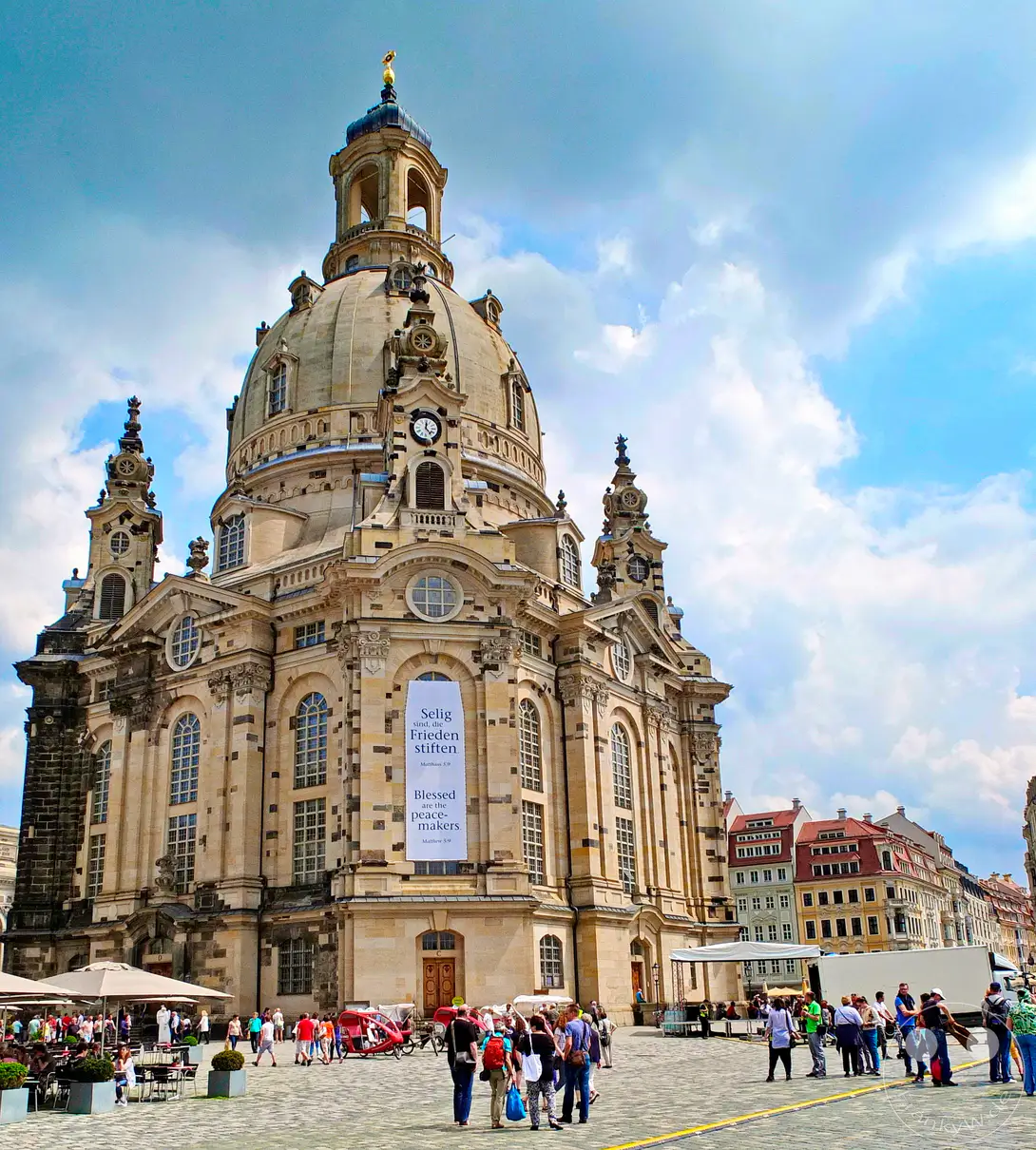 Die beeindruckende Frauenkirche prägt das Stadtbild von Dresden mit ihrer barocken Architektur und imposanten Kuppel. Auf dem davorliegenden Platz herrscht reges Treiben mit Menschen, die die historische Umgebung erkunden. Das atmosphärische Wetter mit dramatischen Wolken verleiht der Szene eine besondere Tiefe.
