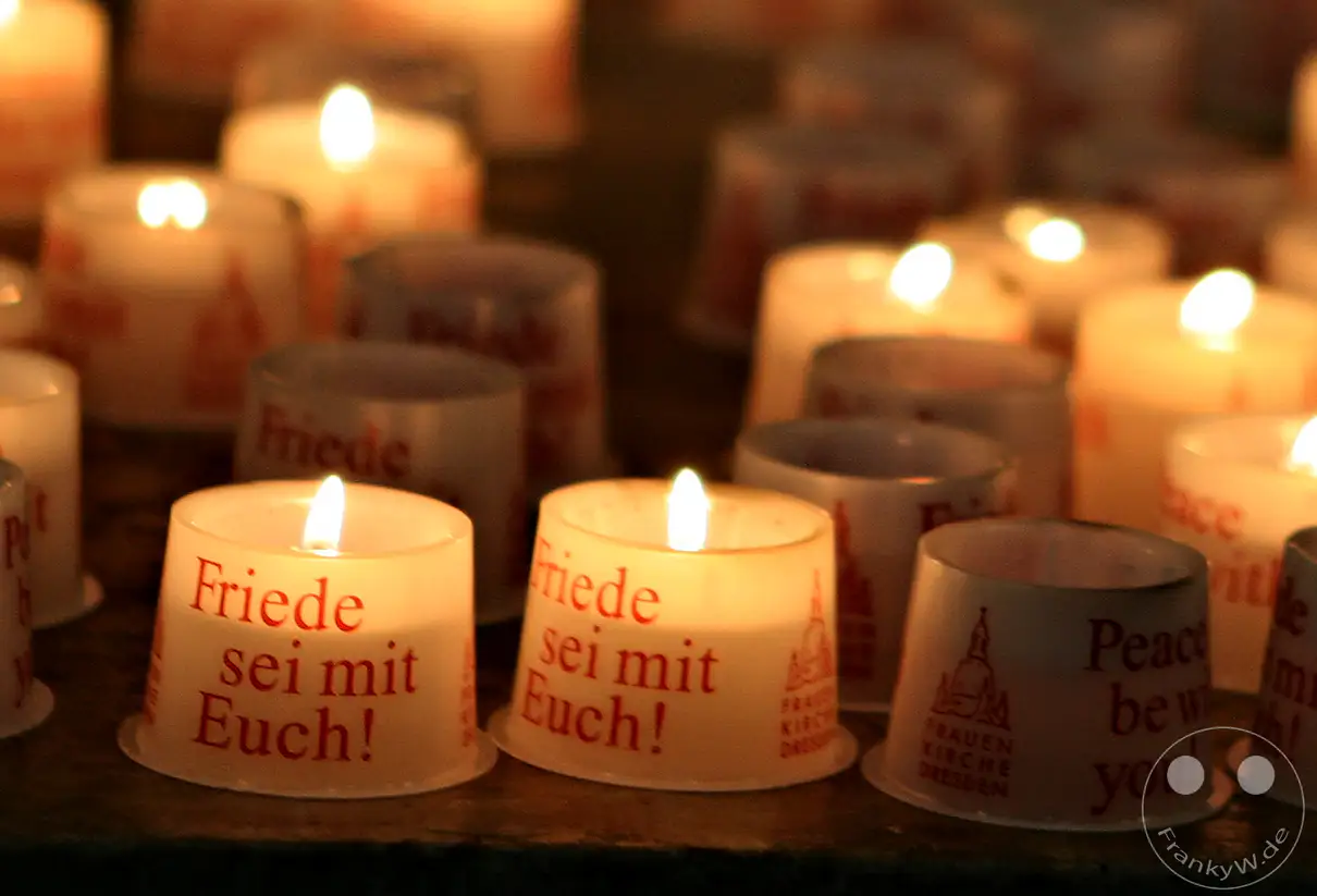 Zahlreiche Kerzen leuchten in der Dunkelheit, einige tragen die Aufschrift "Friede sei mit Euch!" und den Schriftzug "Frauenkirche Dresden". Die Szene strahlt eine friedliche und nachdenkliche Stimmung aus, die zum Gedenken einlädt.