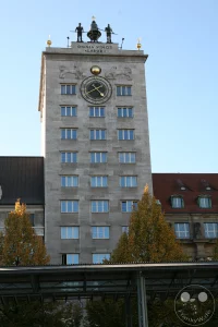 Die markante Steinfassade des historischen Kroch-Hochhauses ragt am Rande des Augustusplatzes empor. Das im Jahr 1928 errichtete Bauwerk gilt als das erste Hochhaus Leipziger Architekturgeschichte und besticht durch sein markantes Turmdach, auf dem zwei bronzene Glockenschläger über der lateinischen Inschrift prangen. Die symmetrisch angeordneten Fensterreihen und die prachtvolle Turmuhr mit goldenen Zeigern verleihen dem geschichtsträchtigen Baudenkmal seine unverkennbare optische Eleganz.
