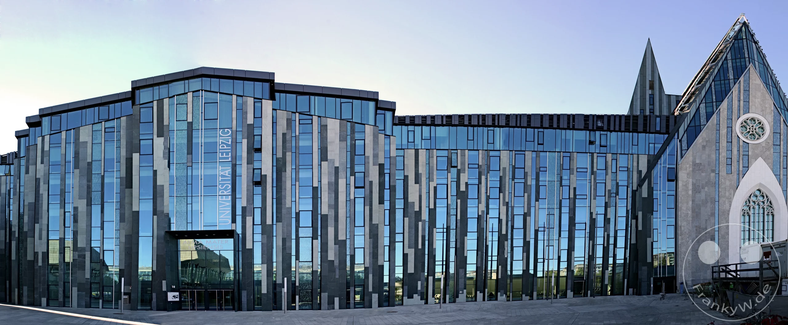 Die moderne Glasfassade der Universität Leipzig trifft auf ein historisches Bauwerk in Deutschland. Die Aufnahme vermittelt einen Eindruck von der imposanten und zugleich stilvollen Architektur des Universitätsgebäudes in Leipzig. Heller Himmel und die glänzenden Oberflächen erzeugen eine klare und fortschrittliche Atmosphäre.
