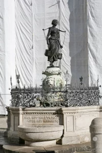 Die detailreiche Bronzefigur einer Wasserträgerin ist als Teil des Mägdebrunnens in Leipzig zu sehen. Die Statue, die über einer kunstvoll verzierten Brunnenkonstruktion thront, vermittelt eine historische und künstlerische Atmosphäre. Ihre Pose und die angedeuteten Wasserkrüge erzählen von der Bedeutung des Wassers für vergangene Zeiten in Deutschland.