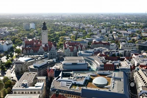 Eine weitläufige Ansicht der Stadt Leipzig in Deutschland erfasst die historische Architektur, darunter das imposante Neue Rathaus, neben modernen Gebäuden und viel Grün. Die urbane Szenerie bietet einen Eindruck von der Vielfalt und Dichte des Stadtzentrums. Die Szene ist von einem erhöhten Aussichtspunkt aufgenommen, was die Weite der Stadt und ihre bauliche Entwicklung unterstreicht.