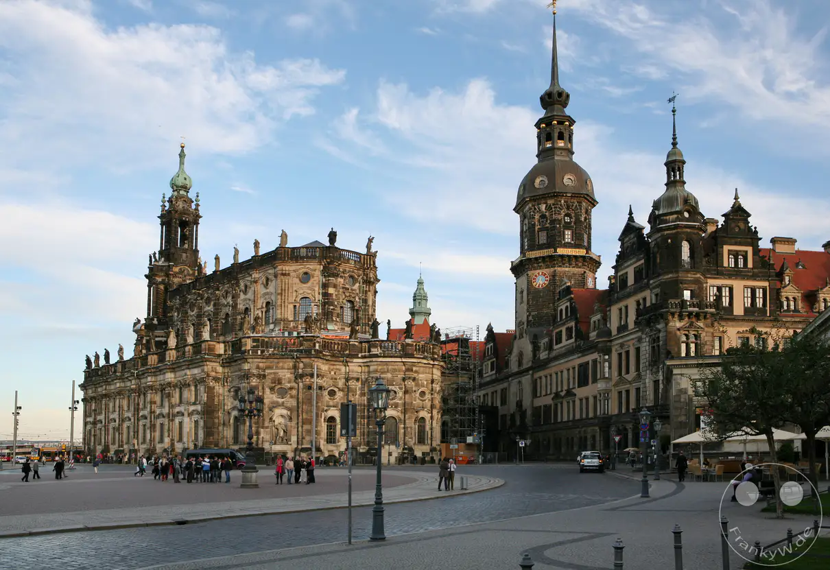 Die barocke Katholische Hofkirche, heute Kathedrale Sanctissimae Trinitatis, bildet zusammen mit dem angrenzenden Residenzschloss das Herzstück des historischen Theaterplatzes. Der prächtige Kirchenbau wurde im 18. Jahrhundert unter Kurfürst Friedrich August II. durch den italienischen Architekten Gaetano Chiaveri errichtet und ist für seine mit Heiligenstatuen geschmückte Balustrade bekannt. Direkt daneben ragt der Hausmannsturm des Dresdner Residenzschlosses empor, welches über Jahrhunderte der Regierungssitz der sächsischen Kurfürsten und Könige war. Dieses weltberühmte Bauensemble prägt maßgeblich das historische Stadtbild der sächsischen Landeshauptstadt an der Elbe.