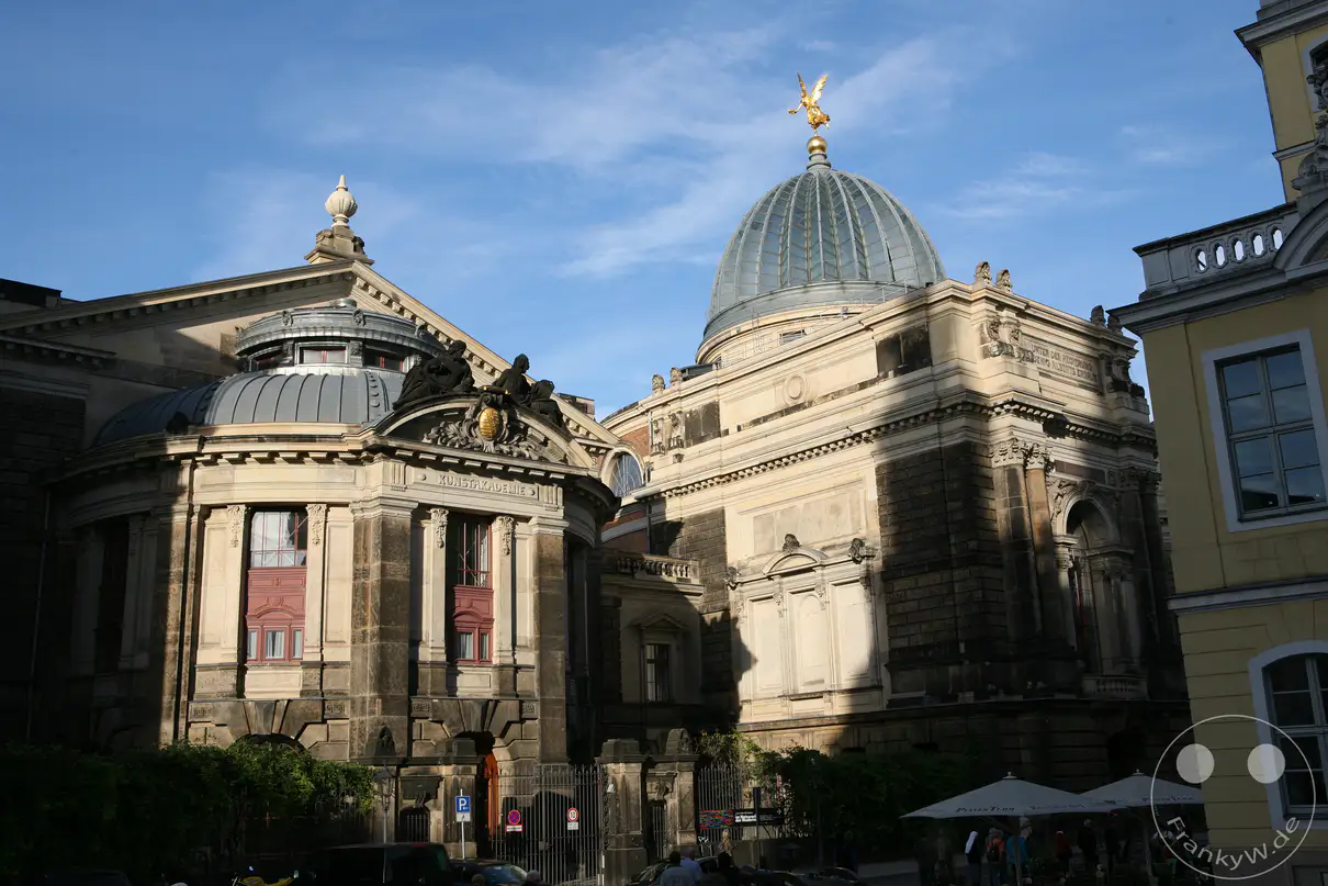 Die charakteristische Glaskuppel der Dresdner Kunstakademie wird wegen ihrer gefalteten Form im Volksmund liebevoll als „Zitronenpresse“ bezeichnet und trägt an ihrer Spitze eine goldene Fama-Figur. Der monumentale Gebäudekomplex an der Brühlschen Terrasse wurde Ende des 19. Jahrhunderts im Stil des Historismus unter der Leitung von Constantin Lipsius errichtet. Auf der rechten Seite ist die Seitenansicht des prächtigen Kopfbaus zu sehen, der zur Frauenkirche ausgerichtet ist. Das Gesamtensemble prägt bis heute die weltberühmte Silhouette der Dresdner Altstadt.