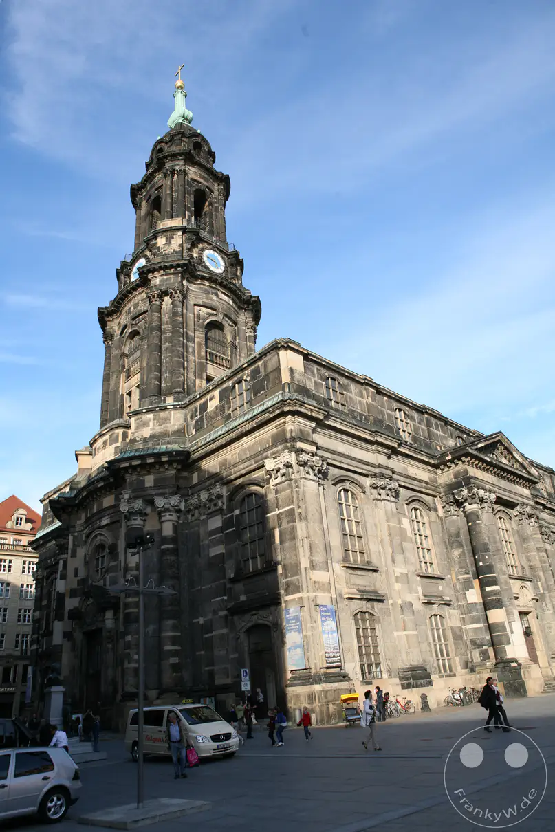 Die historische Kreuzkirche in Dresden überragt mit ihrem markanten, dunkelgrauen Sandsteinturm den weitläufigen, von Passanten belebten Platz unter einem leicht bewölkten, blauen Himmel. Die imposante Architektur im Stil des Spätbarocks und Klassizismus strahlt eine zeitlose, monumentale Ruhe aus, während das helle Tageslicht starke Kontraste auf der detailreichen Fassade erzeugt. Alltagsszenen mit Fußgängern und einem vorbeifahrenden Transporter verleihen der urbanen Kulisse in Deutschland eine lebendige und zugleich beständige Atmosphäre.