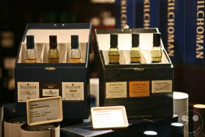 Zwei exklusive Whisky-Geschenkpackungen namhafter schottischer Brennereien präsentieren sich in der feinkostorientierten Ladenpassage des Leipziger Messepalastes Specks Hof. Das linke Set enthält drei Miniaturflaschen der Destillerie Talisker mit den Editionen 10 Jahre, Distillers Edition und 57° North, untermalt von einem detaillierten Preisschild für Feinschmecker im Vordergrund. Direkt daneben steht das Probierset der Caol Ila Collection mit drei verschiedenen Single-Malt-Abfüllungen der schottischen Insel Islay, während im Hintergrund blaue Verpackungen von Kilchoman das hochwertige Spezialitätensortiment für Genießer abrunden.