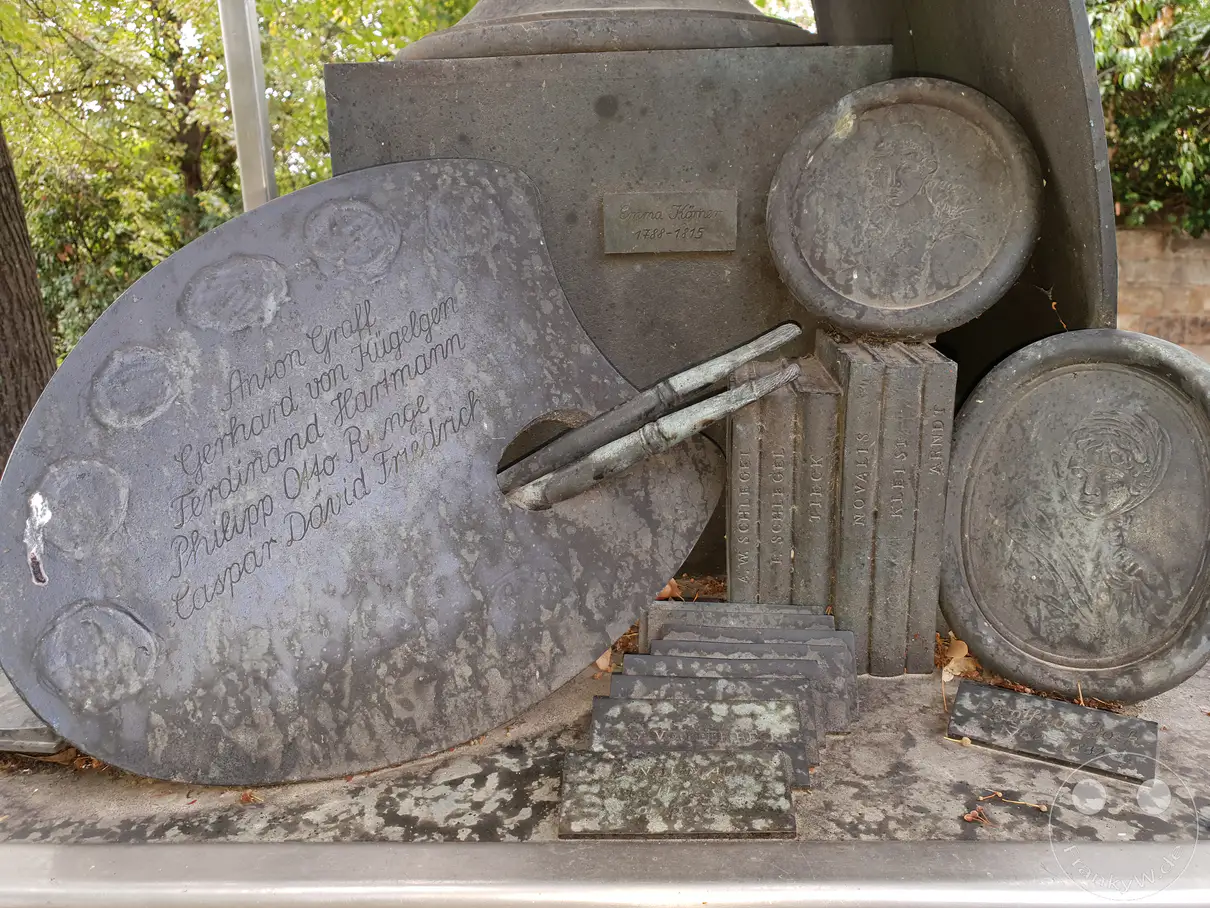 Die bronzene Malerpalette als Teil einer dreiteiligen Denkmalgruppe ehrt berühmte Künstler des romantischen Zeitalters vor dem Kügelgenhaus in Dresden. Das detailreiche Kunstwerk an der belebten Hauptstraße erinnert mit eingravierten Künstlernamen, Pinseln, historischen Buchrücken und Porträtmedaillons an die reiche Kulturgeschichte in Deutschland. Eine ehrwürdige, geschichtsträchtige und kulturell inspirierende Stimmung geht von dieser skulpturalen Installation im Außenbereich aus.