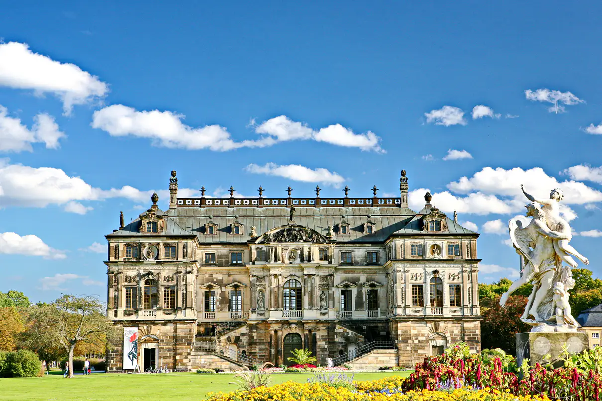Das Palais im Großen Garten in Dresden repräsentiert ein prachtvolles Lustschloss im barocken Stil. Die weitläufige Grünanlage und die kunstvollen Skulpturen vor der beeindruckenden Fassade erzeugen eine Atmosphäre von historischer Eleganz und Ruhe. Dieser Ort lädt zum Flanieren und zur Bewunderung der sächsischen Architekturgeschichte ein.