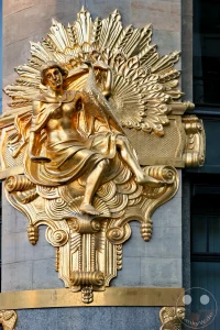 Das prachtvolle und detailreich vergoldete Jugendstil-Relief an der Fassade des ehemaligen Kaufhauses Ebert am Thomaskirchhof zeigt die Allegorie der Eitelkeit (Superbia). Die sitzende weibliche Figur hält einen kleinen Handspiegel in ihrer rechten Hand und blickt andächtig zu einem majestätischen Pfau empor, der vor einem strahlenförmigen Fächerhintergrund seine Federn präsentiert. Dieses beeindruckende, im Sonnenlicht glänzende Kunstwerk fängt das handwerkliche Geschick der Jahrhundertwende ein und erinnert augenzwinkernde an den ursprünglichen Zweck des Gebäudes als exklusives Modewarenhaus