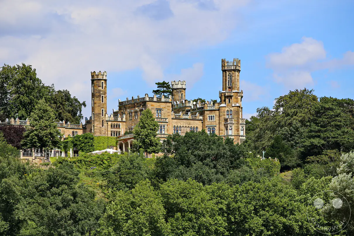 Schloss Eckberg thront majestätisch auf einem Hügel oberhalb der Elbe bei Dresden und ist umgeben von üppiger Vegetation. Das historische Gebäude mit seinen markanten Türmen und der steinernen Fassade strahlt eine romantische und erhabene Atmosphäre aus. Ein idyllischer Ort, der Geschichte und Natur auf beeindruckende Weise vereint.