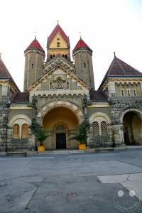 Die monumentale, neuromanische Westfassade der historischen Kapellenanlage erhebt sich eindrucksvoll auf dem Leipziger Südfriedhof. Das zwischen 1907 und 1910 nach Plänen des Stadtbaurats Otto Wilhelm Scharenberg errichtete Bauensemble besticht durch seine massiven Sandsteinfronten, die charakteristischen Rundbogenportale und die markanten spitzen Turmpyramiden. Im Zentrum des gepflasterten Vorplatzes führt ein großes, schattiges Eingangsportal zum Trauerhallen-Komplex, welcher gestalterisch stark von der romanischen Abtei Maria Laach inspiriert wurde und heute als architektonisches Kernstück des geschützten Parkfriedhofs gilt.