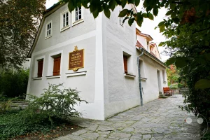 Das Schillerhaus in Leipzig, das älteste erhaltene Bauernhaus der Stadt, erinnert an den Aufenthalt Friedrich Schillers. Eine Gedenktafel informiert über seine Zeit hier im Jahr 1785, als er das Drama "Don Karlos" vollendete. Der historische Ort strahlt eine stille, nachdenkliche Atmosphäre aus, umgeben von einem gepflasterten Weg und grüner Vegetation.