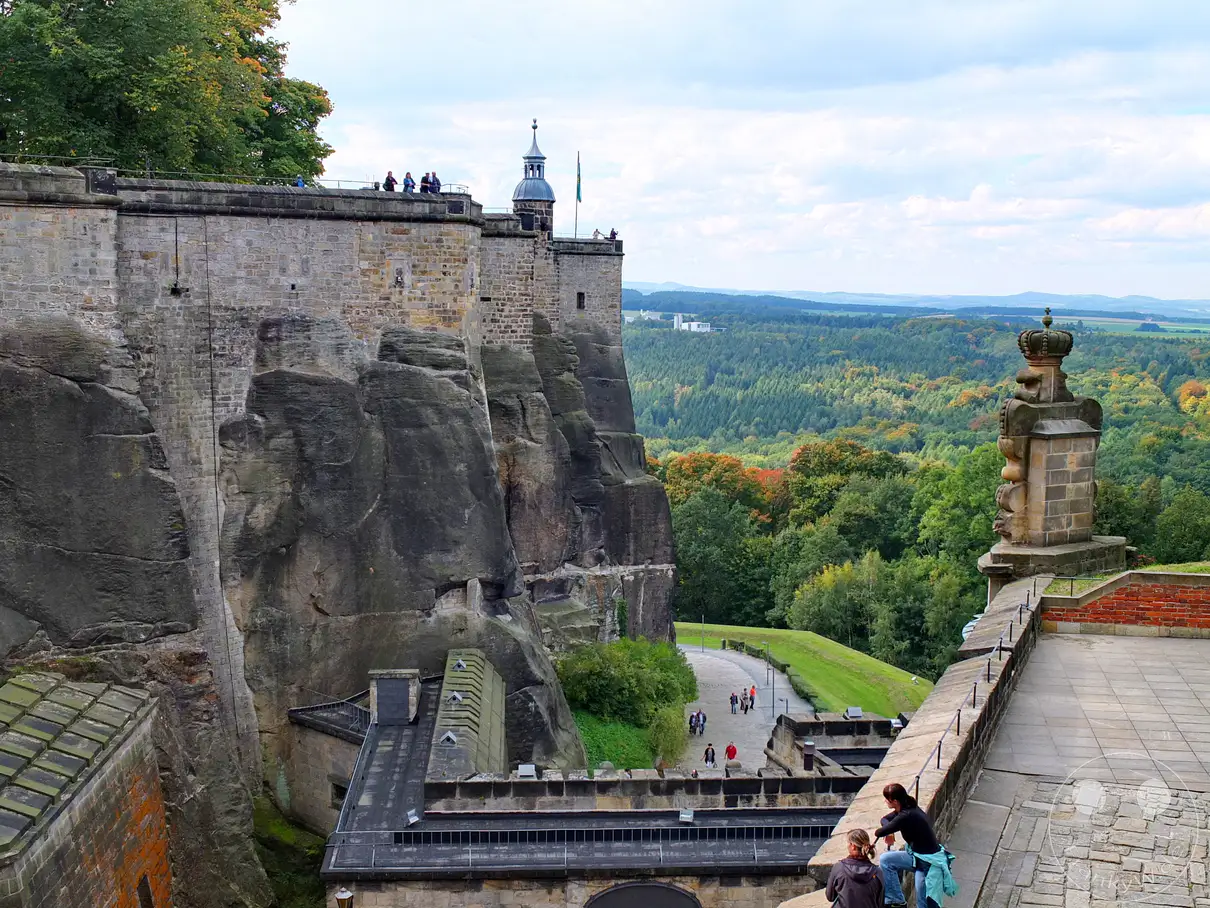 Die imposante Festung Königstein thront auf einem Tafelberg und bietet einen atemberaubenden Panoramablick über die sächsische Schweiz. Besucher schlendern entlang der weitläufigen Festungsmauern und genießen die herbstliche Landschaft. Die historische Anlage strahlt Ruhe und Erhabenheit aus, während die weite Natur zum Verweilen einlädt.