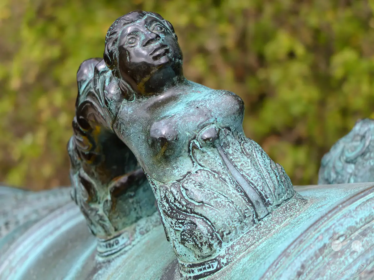 Eine stark vergrößerte Ansicht einer alten Belagerungskanone auf der Festung Königstein in der Sächsischen Schweiz, Deutschland. Die bronzene Skulptur ist mit einer grünlichen Patina überzogen und zeigt die Darstellung eines Delphins, dessen Henkel eine kunstvolle Verzierung aufweisen. Die Aufnahme vermittelt einen Eindruck von der detailreichen Handwerkskunst und dem historischen Charakter dieser militärischen Anlage.