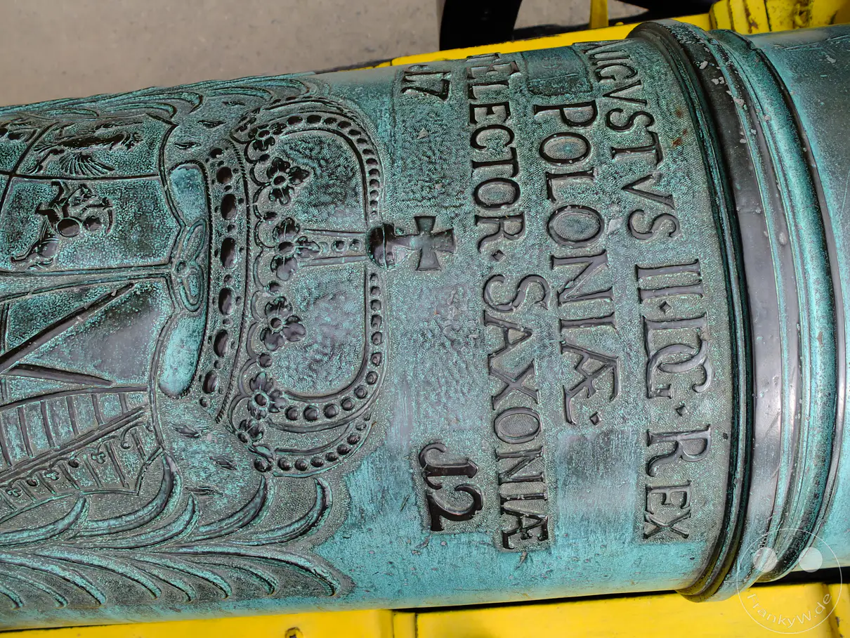 Detailaufnahme einer alten Belagerungskanone auf der Festung Königstein in der Sächsischen Schweiz, Deutschland. Die kunstvollen Gravuren und die Patina auf dem bronzenen Geschütz zeugen von seiner reichen Geschichte und militärischen Bedeutung. Die Verwitterung und die markante grüne Patina verleihen der Kanone eine eindrucksvolle und historische Ausstrahlung.