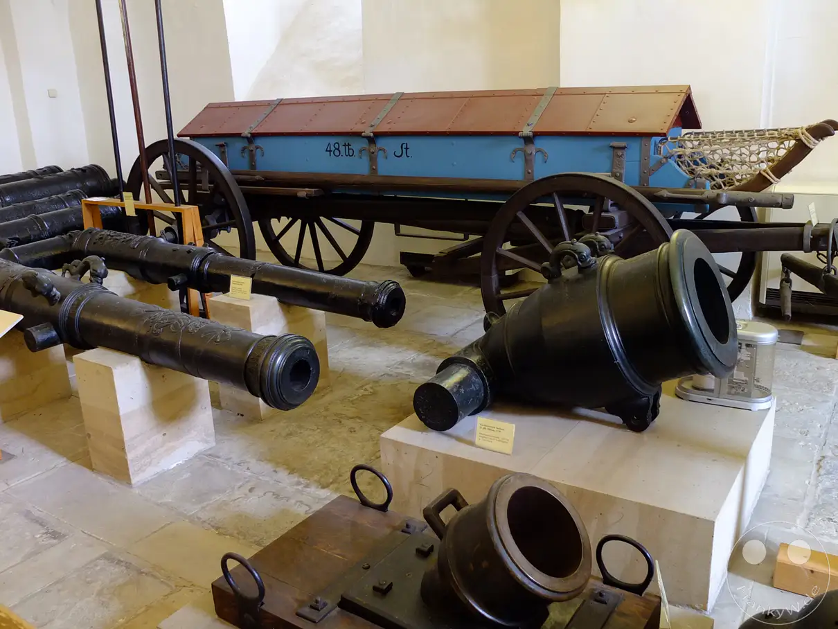 Im Inneren des Alten Zeughauses auf der Festung Königstein in der Sächsischen Schweiz sind historische Kanonen und Geschütze ausgestellt. Ein blau-roter Munitionswagen steht im Hintergrund und ergänzt die beeindruckende militärische Sammlung. Die Szene vermittelt einen Eindruck von vergangener Wehrhaftigkeit und der technischen Entwicklung der Artillerie.