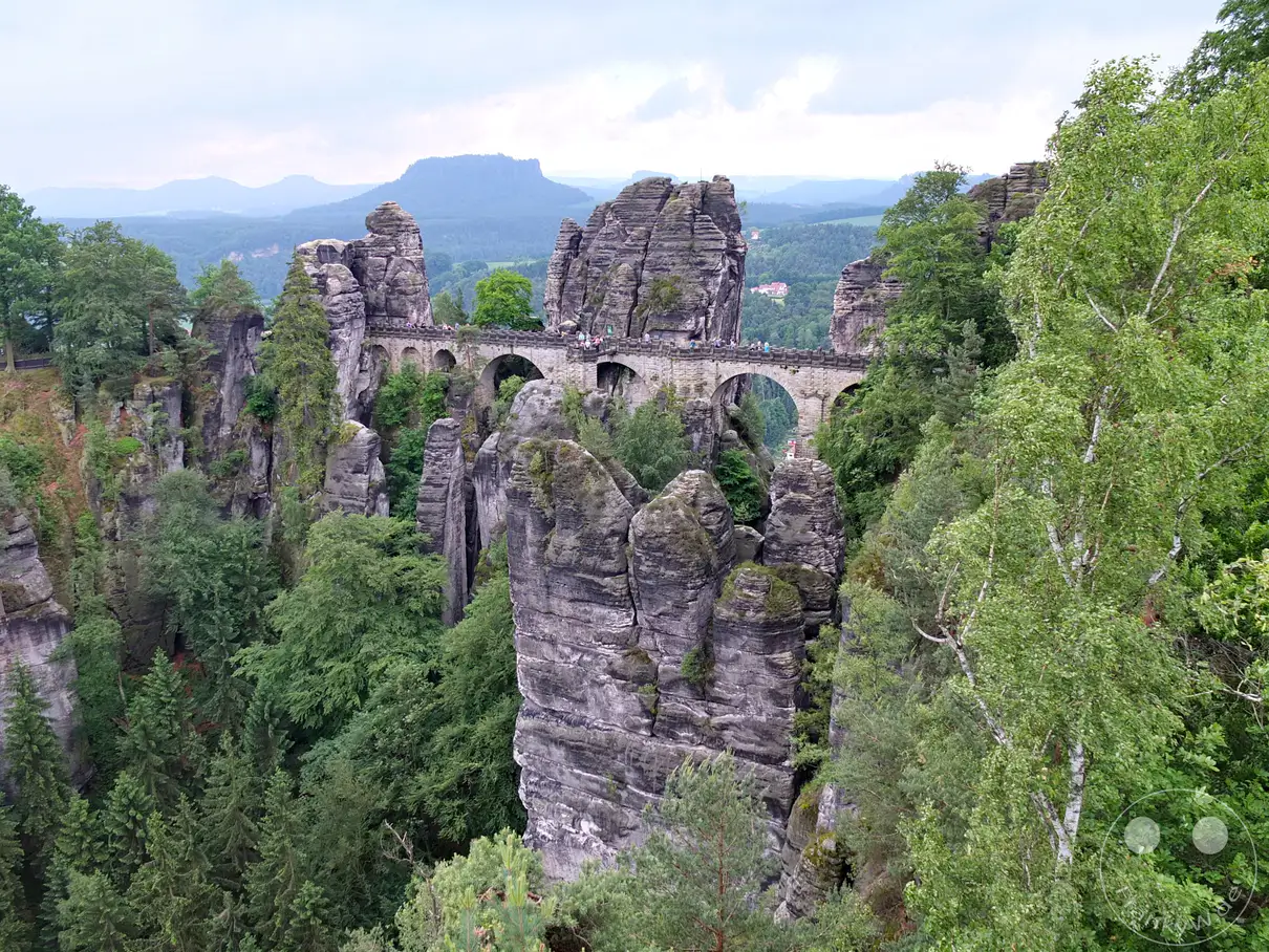 Die Basteibrücke überspannt majestätisch eine Schlucht in der Sächsischen Schweiz und verbindet beeindruckende Felsformationen. Umgeben von üppigem Grün und tiefen Wäldern bietet sich ein atemberaubender Panoramablick auf die zerklüftete Landschaft. Die Szenerie strahlt eine friedliche Ruhe und die ungezähmte Schönheit der deutschen Natur aus.