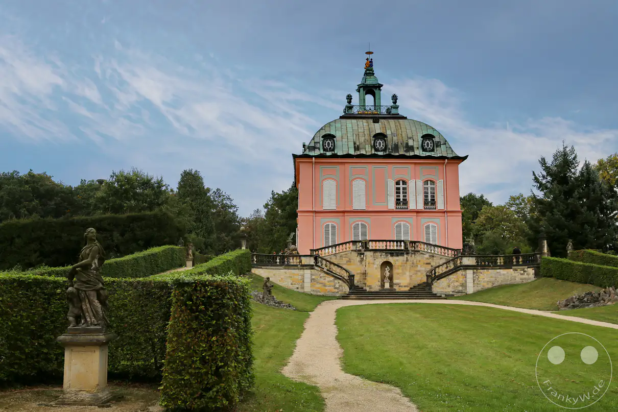 Das Fasanenschlösschen in Moritzburg, Deutschland, präsentiert sich majestätisch im barocken Park, umgeben von kunstvoll geschnittenen Hecken und historischen Statuen. Die Architektur des Schlösschens, mit seiner pastellrosa Fassade und dem grünen Kuppeldach, spiegelt die prunkvolle Gartenkunst der Epoche wider. Eine bepflasterte Wegeführung lädt den Betrachter ein, die friedliche und erhabene Atmosphäre dieses geschichtsträchtigen Ortes zu erkunden.